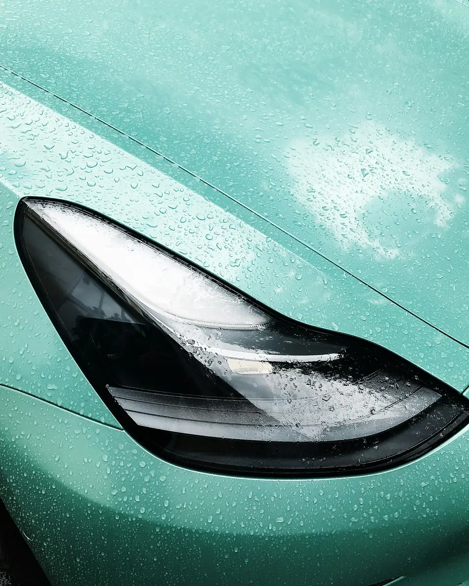 Lluvia en gotas sobre un capó verde menta junto al faro