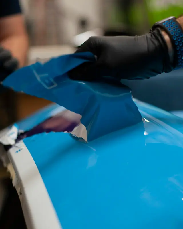 Manos con guantes alisando una lámina sobre un capó azul
