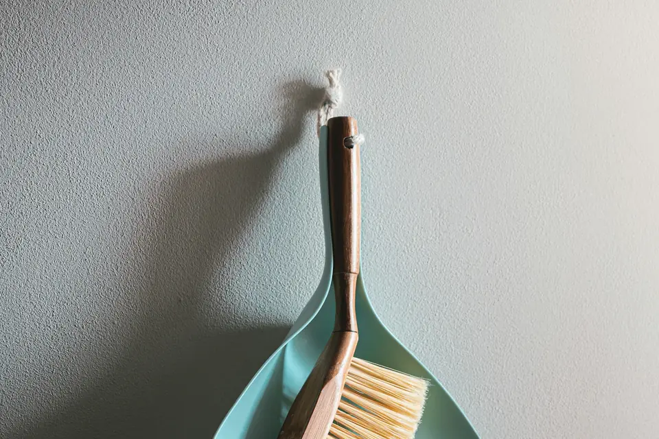 Cepillo de madera y recogedor verde menta colgados en una pared blanca