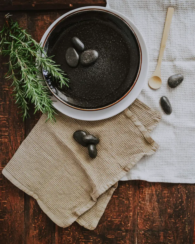 Black massage stones in a dark bowl with rosemary and linen cloths on old wood