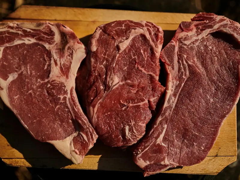 Three thick marbled ribeye steaks on a wooden board