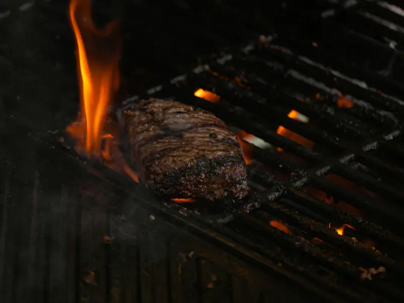 Skirt steak on the grate with a flame rising beside it
