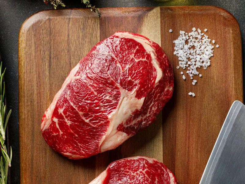 Two marbled ribeye steaks on a board with salt and rosemary