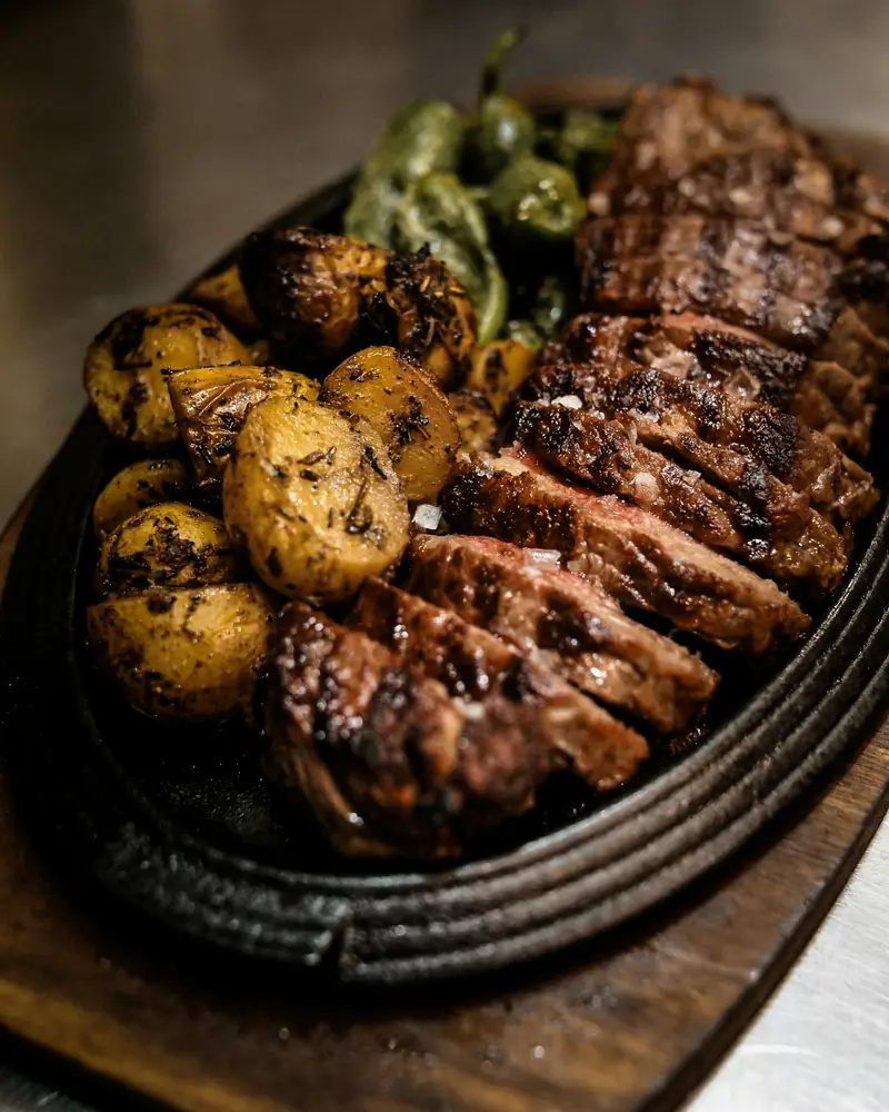 Sliced steak with herbed potatoes and peppers on a cast-iron platter