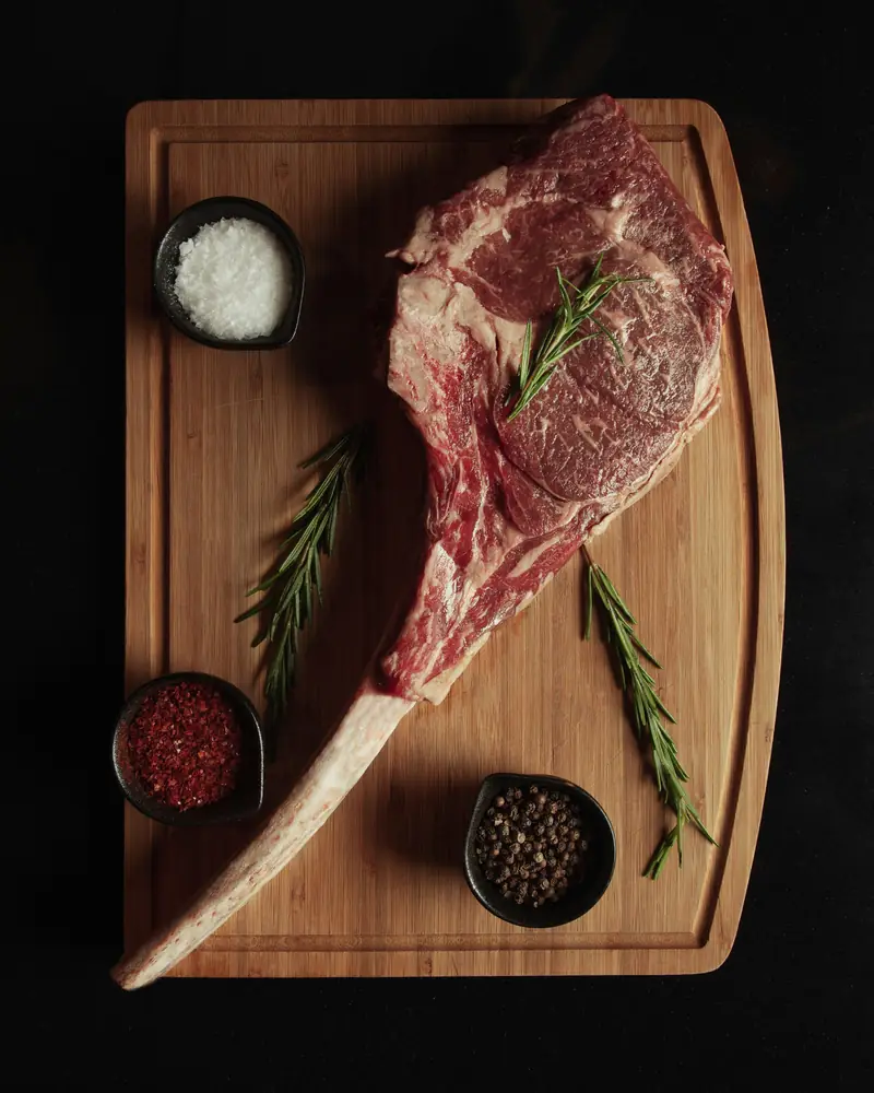 A raw tomahawk steak with rosemary and spices on a board