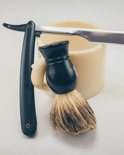 Straight razor and shaving brush leaning on a cream shaving mug