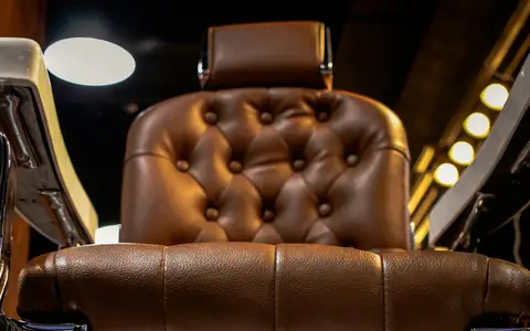 Low view of a tufted brown leather barber chair with chrome arms