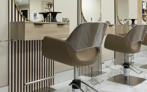 Studio stations with arched mirrors, slatted panels and beige chairs on a marble floor