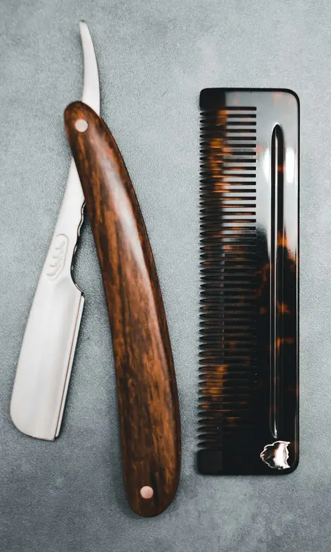 Straight razor with a wooden handle beside a tortoiseshell comb on grey stone