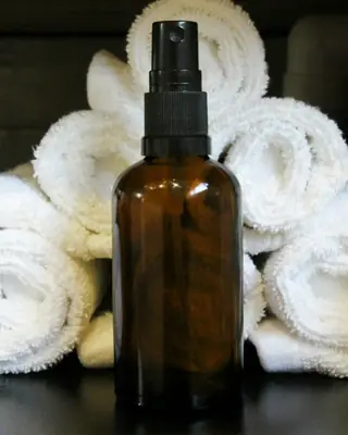 Amber glass spray bottle in front of rolled white towels