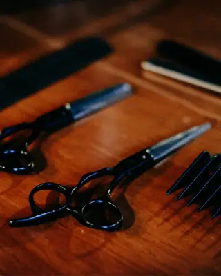 Black scissors, combs and a razor laid out on a warm wooden counter