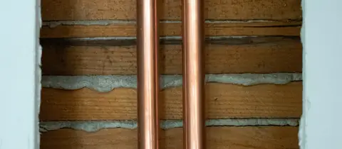 Two new copper pipes running up an opened wall, fixed to the brickwork before it is closed