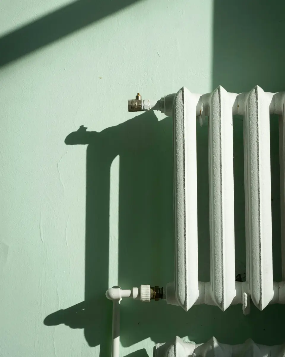 A white radiator and its valve on a mint wall in the sun