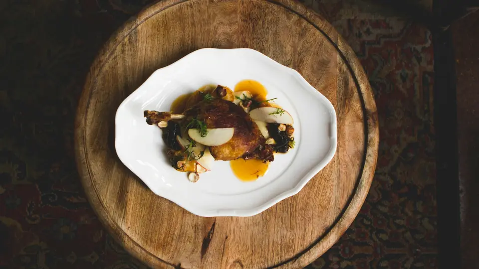 Pato asado con su jugo brillante, emplatado sobre una tabla redonda de madera