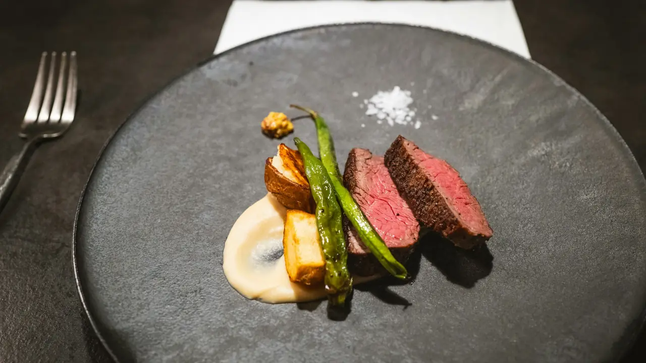 Ternera en láminas con judías verdes tostadas y puré fino sobre un plato de piedra oscura