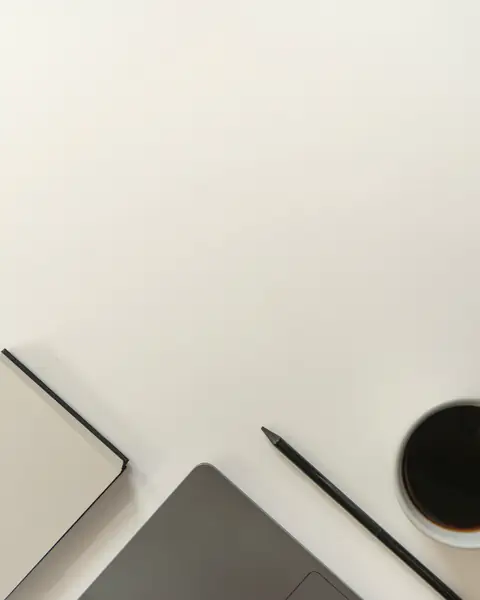 Laptop, notebook, pencil and coffee on a white desk from above