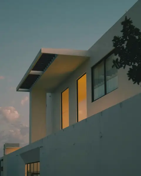 White modern house with warm lit windows against a dusk sky
