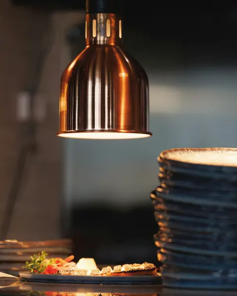 Copper heat lamp over a plated dish at the kitchen pass