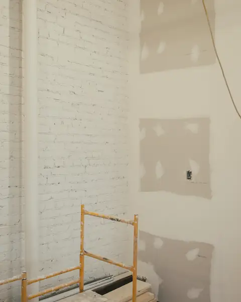 New plasterboard patches beside a painted brick wall and a scaffold